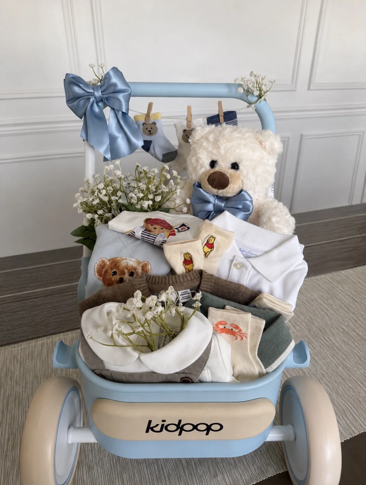 Blue baby basket wagon with teddy bear, bow, florals, and baby clothing