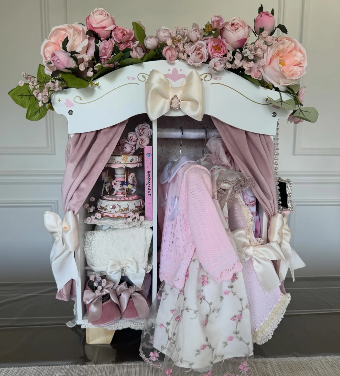 Luxury baby wardrobe gift display with florals, bows, and keepsake clothing